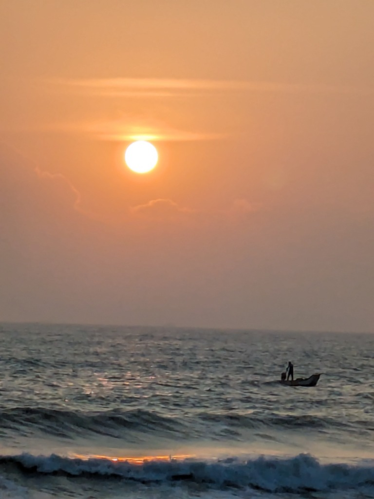 Orange sun setting over the sea with a small boat on the water