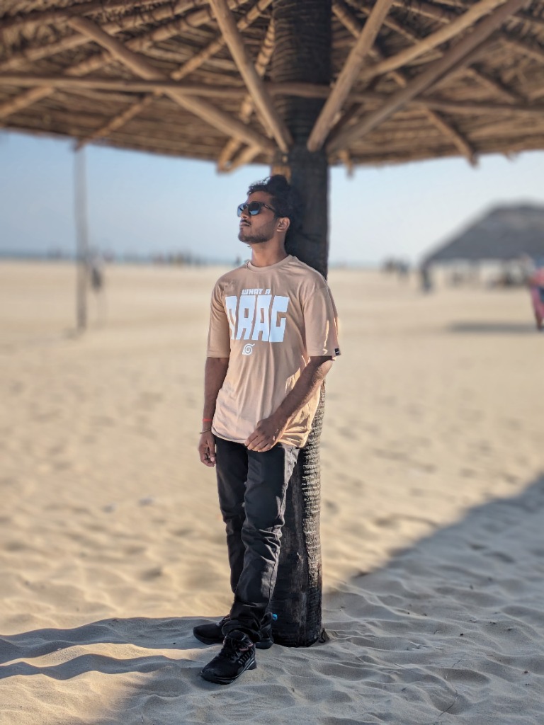 Man in sunglasses standing under a thatched umbrella on a sandy beach